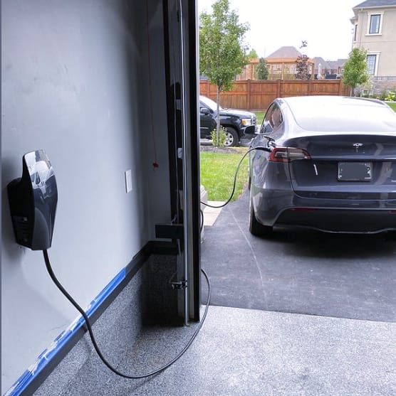 A home EV charging station mounted on an exterior wall with a car parked nearby