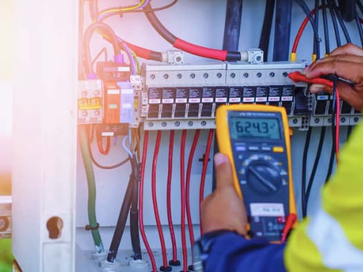 A Pica electrician wiring an electrical panel with a multimeter in hand